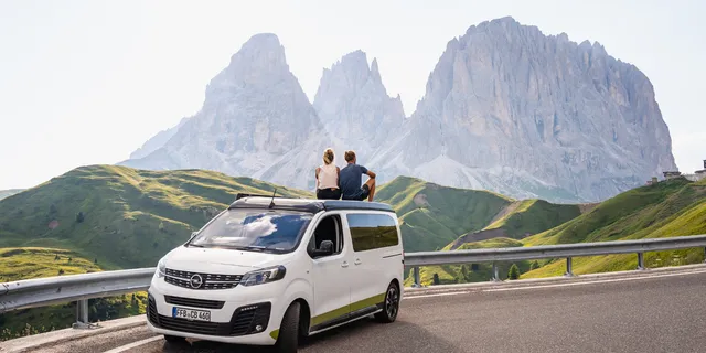 Two people are sitting on a camper in the Dolomites