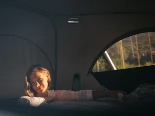 A woman stands at Alpsee Camping in a camper and builds the roof bed.