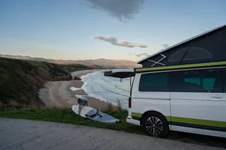Holiday in April in the Algarve: A woman with surfboard next to her camper off the coast and mountain landscape of Portugal
