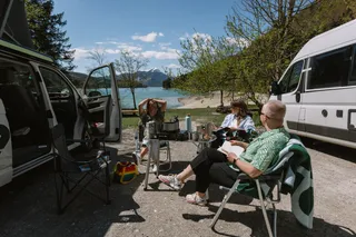 Three friends at Camping am See in Bavaria sitting on a camping table on the shore