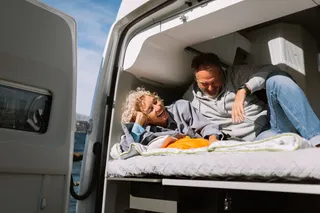 A holiday in April: A couple is next to each other in the camper in the sun and laughs cordially